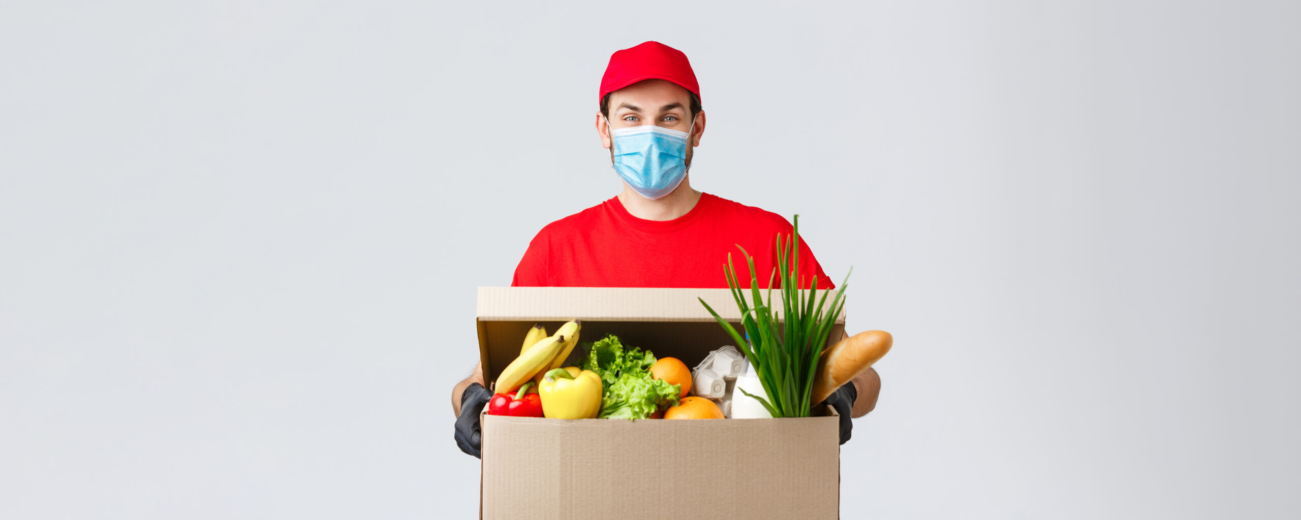 ClicknCollect courier in red outfit holding a box of groceries including bananas, lettuce, peppers, and bread.