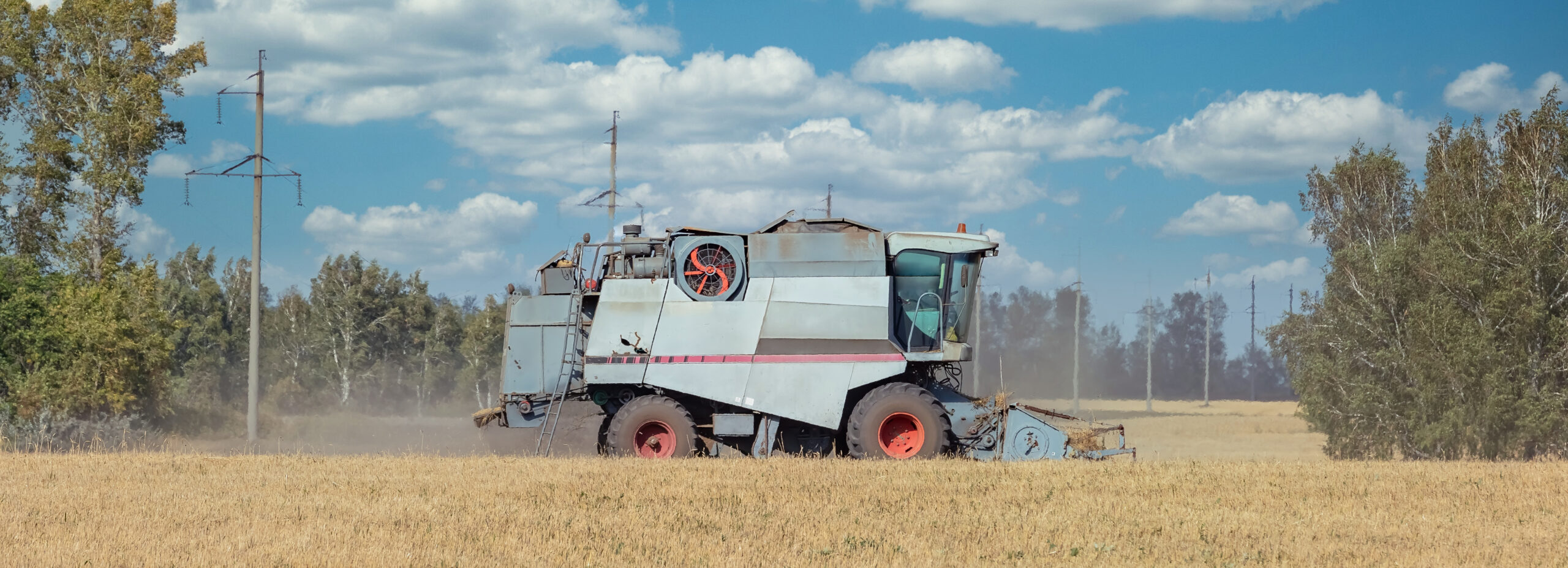 A combine harvester cuts wheat in a field under a clear blue sky with scattered clouds. Mentioning Khaity, the image illustrates modern farming efficiency.