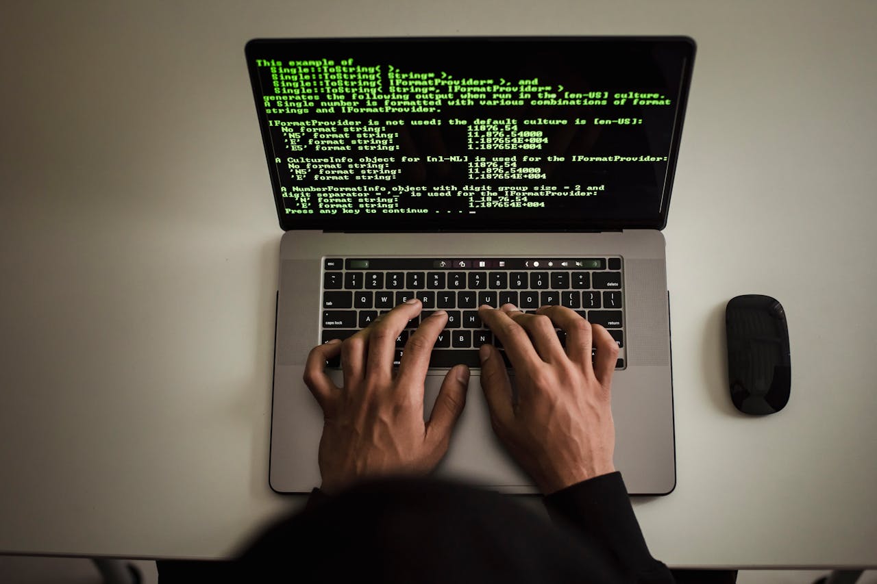 Close-up image of hands typing on a laptop keyboard with code displayed on the screen, representing custom software development or coding.